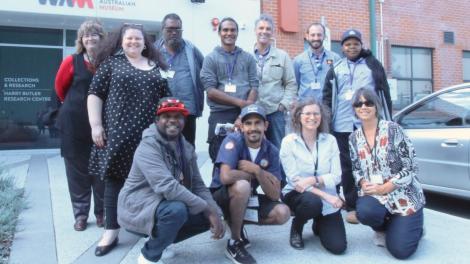 "A group of people post for a photo outside a building, a row of four people kneel at the front while the rest of the group stands behind them."